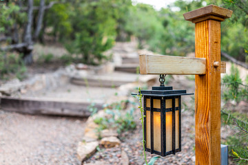 Japan in evening with illuminated hanging lantern lamp light on wooden pole post in Japanese garden with steps stairs and green trees foliage in blurry blurred background