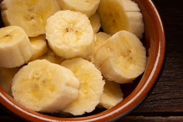 A banch of bananas and a sliced banana in a pot over a wooden table.