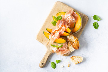 Fresh melon with prosciutto and basil. Antipasti, Italian food. Top view on white stone table with...