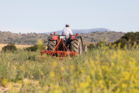 Agricultor en tractor rojo arando la tierra en el campo para sembrar un cultivo de cereales