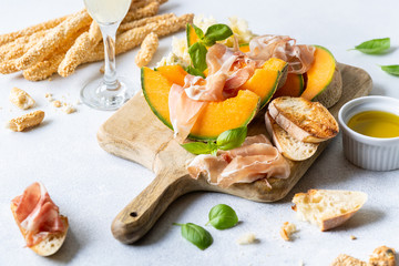 Fresh melon with prosciutto and basil. Antipasti, Italian food. Top view on white stone table with...