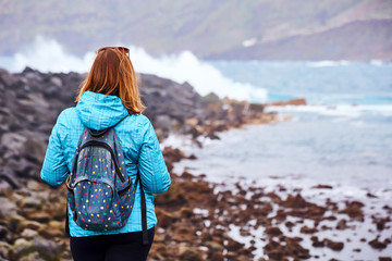 Woman tourist with backpack standing on the quay and watching the ocean in Puerto de la Cruz, The...
