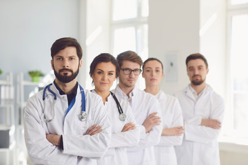 A group of confident practicing doctors cross arms in white coats are smiling in the clinic.