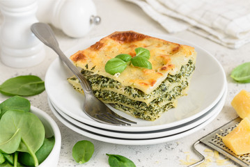 A piece of lasagna with spinach, ricotta and bechamel sauce on a white plate. Traditional italian dish. Selective focus.