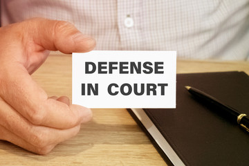 Man hand holding card with the word defense in court. cutting expenses and costs concept.