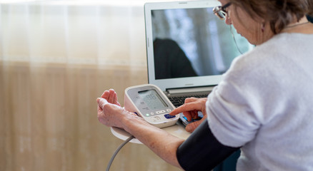 Fototapeta na wymiar telemedicine concept elderly woman using laptop and taking her blood pressure