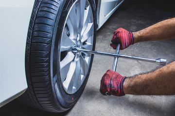 Car mechanic hand using cross wrench to uninstallation the wheel nuts for changing alloy wheel of car in vehicle repair shop.