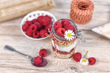 Healthy raspberry fruit dessert with skyr yogurt,  granola and puffed quinoa grains layered in jar surrounded by ingredients