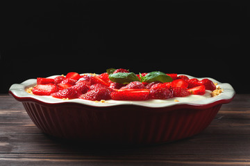 Strawberry cheesecake with basil leaves, in a red ceramic baking dish on a wooden background