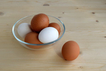 The curine raw eggs are in a glass bowl. Eggs are white and brown. The bowl is on a wooden table.