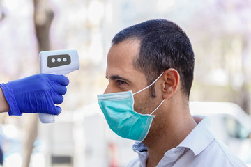 A uomo moro con mascherina chirurgica viene presa la temperatura del corpo con termometro elettronico digitale, isolato su sfondo urbano