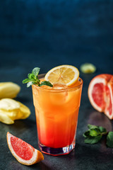 Fresh tropical cocktail with pineapple, grapefruit and ice in glass on dark blue background. Summer cold drink