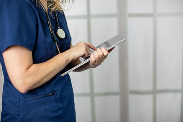 Female medical professional wearing scrubs using technology by writing patient notes on a tablet computer