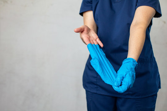 A Medical Health Care Worker Woman In Navy Blue Scrubs Taking Off Her Latex Surgical Gloves The Correct Way Folding Them Inside Out For Preventing The Spread Of Germs And Disease