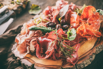 Antipasto platter cold meat plate with prosciutto, slices ham, salami, decorated with basil and olive on dark wooden background. Meat appetizer, set of wine, close up, toning