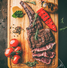 Grilled tomahawk meat medium rare or rib eye steak on wooden cutting board with grilled vegetables...