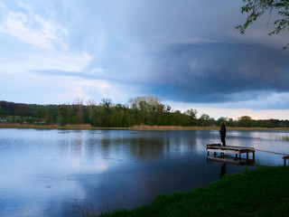 Man fishing under Heavy Stormy sky clouds. Ominous dramatic sky lanscape view over the river