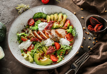 Healthy salad with fillet chicken, avocado, tomatoes, lettuce, greens, pine nuts and sauce in bowl on wooden background. Healthy food, clean eating, dieting, Buddha bowl, top view
