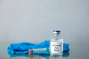 Clear bottle of a clear medicine influenza flu vaccine along with a syringe and surgical gloves with copy space