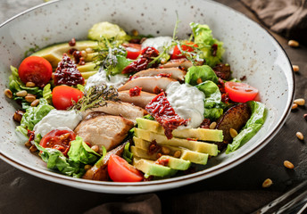 Healthy salad with fillet chicken, avocado, tomatoes, lettuce, greens, pine nuts and sauce in bowl on wooden background. Healthy food, clean eating, dieting, Buddha bowl, top view