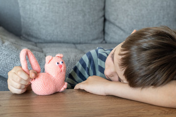 A sad child is playing with a toy pink cat made of yarn. The child plays lying on the table.