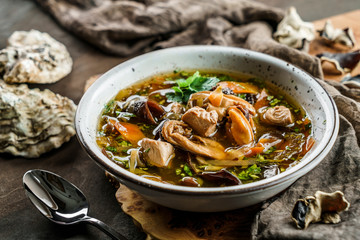 Delicious soup with Black Chinese wood mushrooms and oysters in bowl over wooden background with napkin. Traditional Asian cuisine. Seafood, healthy food, close up