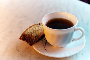 A mug of black coffee with a piece of cake on a plate on a uniform background