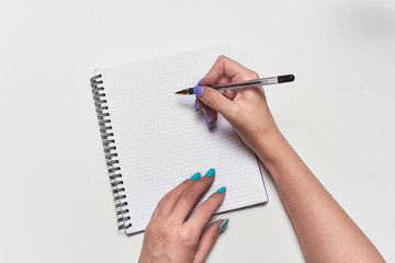 The girl thinks what to write in a notebook, holding a pen, a top view of the hand with a notebook and a pen. Personal diary, records, or business. Blank sheet to fill in