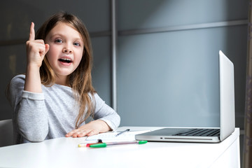Emotions of a child in online classes. Smart girl sitting at the school table with a laptop. Exclamation point.