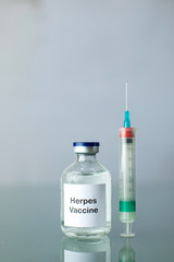 A bottle of a clear medicine herpes vaccine along with a syringe on a plain surface