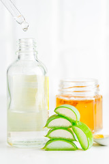 Pipet with drop of homemade lotion from natural aloe vera plant and glass jar with essential oil against light grey background.
