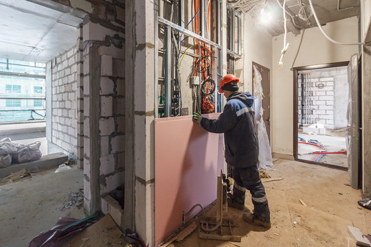 Drywall installation work in progress by construction workers at construction room. Construction worker wear safety uniform installation ceiling work partition for interior wall. New home. 