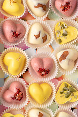 Homemade white chocolate sweets dyed with turmeric extract and heart-shaped strawberry powder with almonds, freeze-dried strawberries and pumpkin seeds. Macro..