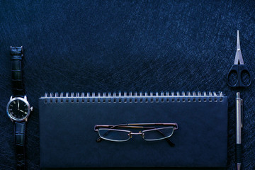.black office supplies: weekly on a spring, watches, pen, scissors and glasses on a black...