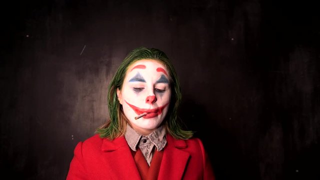 Person in Joker cosplay costume smoking in black office, halloween concept