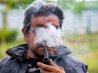 Unshaven Caucasian man in glasses smokes a pipe