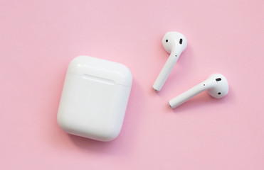 White wireless headphones are on a pink background.
