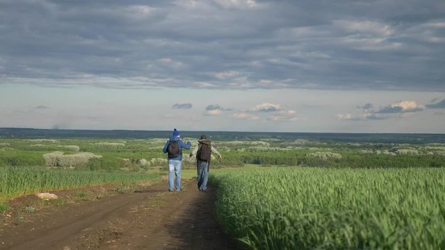 teamwork travel. two man hikers with backpacks walk along a trail next to a field with green grass in nature. concept adventure travel hiking lifestyle healthy. two tourists walk walking talking