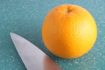 close up of orange fruit with metal knife blade on green board