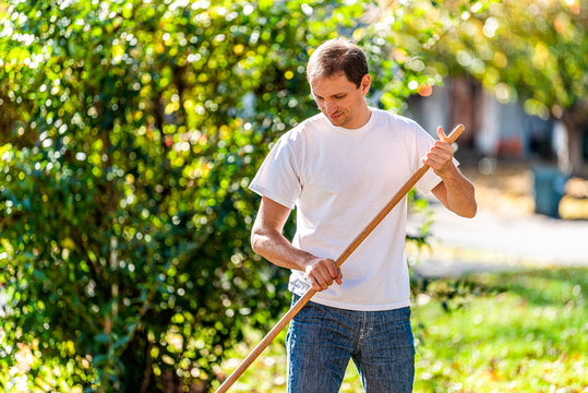 Person homeowner man in garden yard backyard raking autumn leaves standing with rake looking down in fall sunny sunlight outside