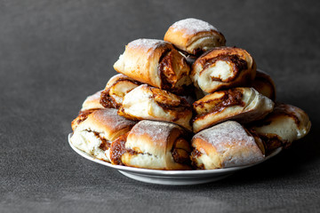 slide of fresh homemade buns with condensed milk and powdered sugar on a plate, on a gray background