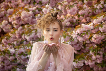 beautiful teenage girl who blows on fallen flowers of sakura tree