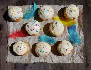 Easter cake cupcake on a wooden table baking paper top view with sprinkles and feathers