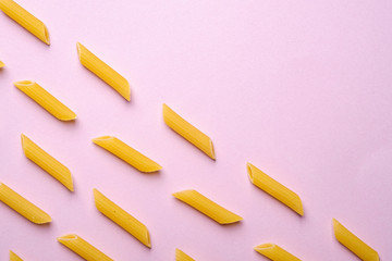 Italian pasta, raw penne tube macaroni pattern on pink background, top view copy space, abstract food