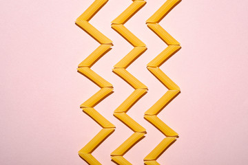 Italian pasta, raw penne tube macaroni zigzag pattern on pink background, top view copy space, abstract food