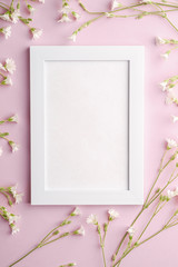 White empty photo frame mockup with mouse-ear chickweed flowers on pink background, top view copy space