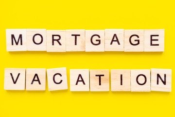 Wooden blocks with the lettering words mortgage vacation on top of yellow background. business and finance concept