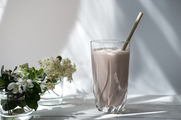 whey drink in a high glass. whey protein chocolate cocktail. aflowers on a white table. morning...