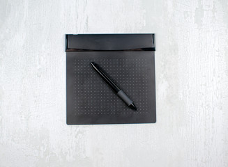 Black graphic digital tablet with pen for illustrators and designers, isolated on a light wood background.