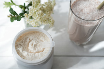 whey drink in a high glass. whey protein chocolate cocktail. a jar with protein powder and flowers on a white table. morning drink for health and beauty. top view